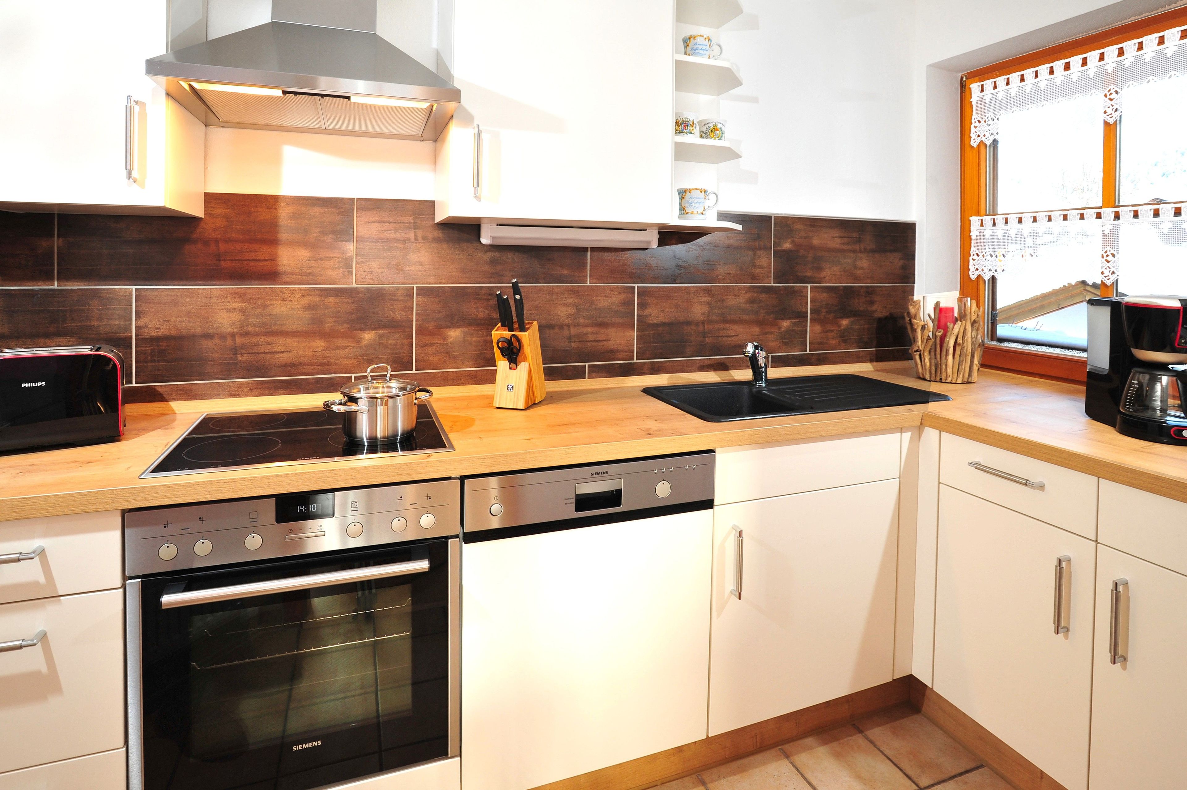 A modern kitchen with a Siemens dishwasher, a Siemens oven, a black Siemens stove, and a wooden countertop.