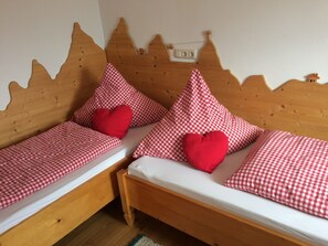 Deux lits en bois, avec une literie à carreaux et des oreillers en forme de cœur rouge.