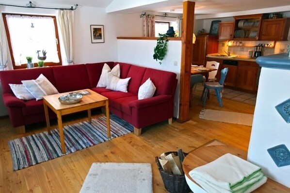 A cozy living room with a red sofa, a wooden coffee table, and a kitchen area visible through an open doorway.
