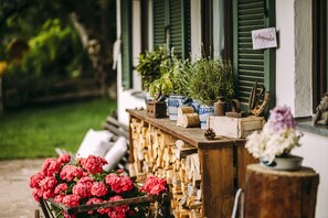 Une table en bois ornée de plantes et de fleurs en pot, une enseigne indiquant « Cottage », et un banc en bois rustique.