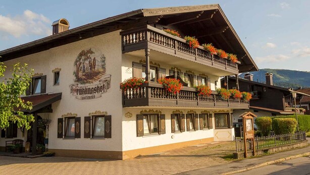 A traditional building with a balcony adorned with flowers, a sign reading "Rülinghof", and a mountain backdrop. - Ein-Raum-Ferienwohnung (3) 27qm, Bad/WC, Küchenzeile, Balkon (Reit im Winkl)