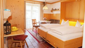 A wooden room with two beds, a table with a lamp, a chair, and a window with curtains. - Ein-Raum-Ferienwohnung (3) 27qm, Bad/WC, Küchenzeile, Balkon (Reit im Winkl)