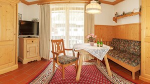 A cozy room with a wooden table, a sofa, a television, and a window with curtains. - Ein-Raum-Ferienwohnung (3) 27qm, Bad/WC, Küchenzeile, Balkon (Reit im Winkl)