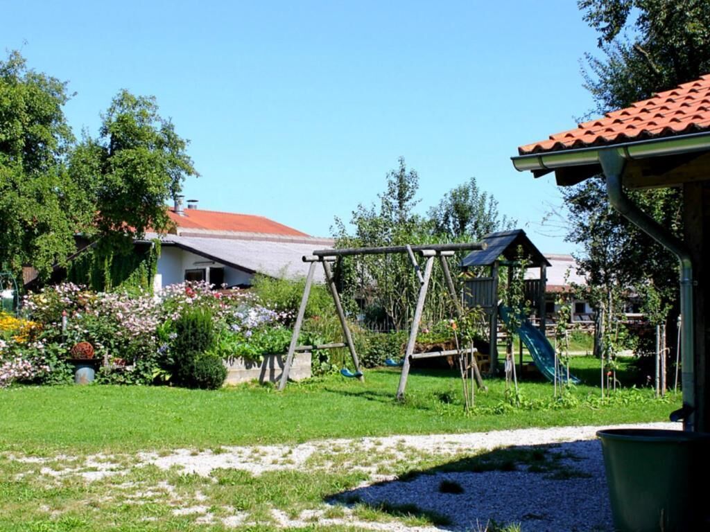 Un jardin avec une balançoire, un belvédère et une maison avec un toit rouge.