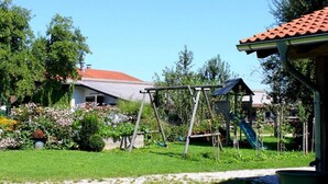Ein Garten mit Schaukel, Laube und einem Haus mit rotem Dach.