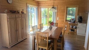 Interior de madera con mesa de comedor, sillas, zona de cocina y un ventanal grande.