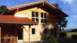 Ein Holzhaus mit geneigtem Dach, einer überdachten Terrasse mit Gartenmöbeln und einem gepflegten Rasen.