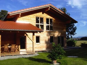 A wooden house with a sloped roof, a covered patio with outdoor furniture, and a well-maintained lawn.