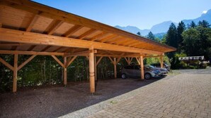 Ein überdachter Parkplatz aus Holz mit geparkten Autos, umgeben von Bäumen und Bergen im Hintergrund.