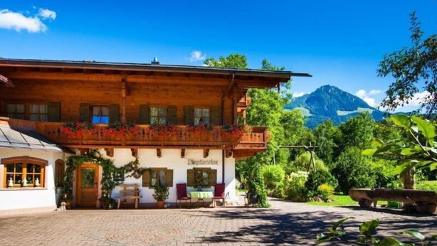 Ein traditionelles Holzhaus mit einem Balkon, einem gepflasterten Innenhof und einem Blick auf die Berge.