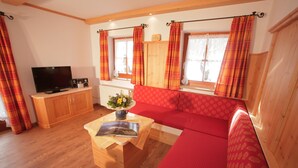 Ein gemütliches Wohnzimmer mit einem roten Sofa, einem Holz-TV-Schrank und einem kleinen Tisch mit Buch und Blumen.