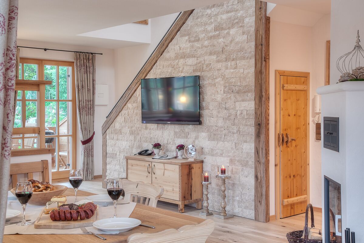 Un coin repas avec une table en bois dressée pour le repas, un meuble en bois sur lequel est posé un téléviseur à écran plat, et un mur en pierre.