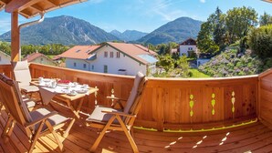 Une terrasse en bois avec une table et des chaises, offrant une vue sur un paysage montagneux parsemé de maisons.