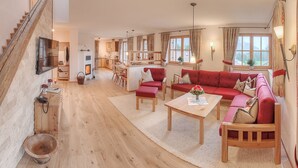 Un salon spacieux avec un ensemble de canapés rouges, une table basse en bois et un escalier.