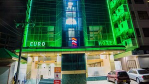Um hotel com um letreiro chamativo 'EURO HOTEL', fachada de vidro e contorno de neon verde.
