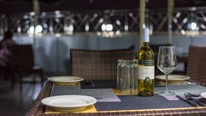 Mesa posta para refeição, com garrafa de vinho, copos e pratos.