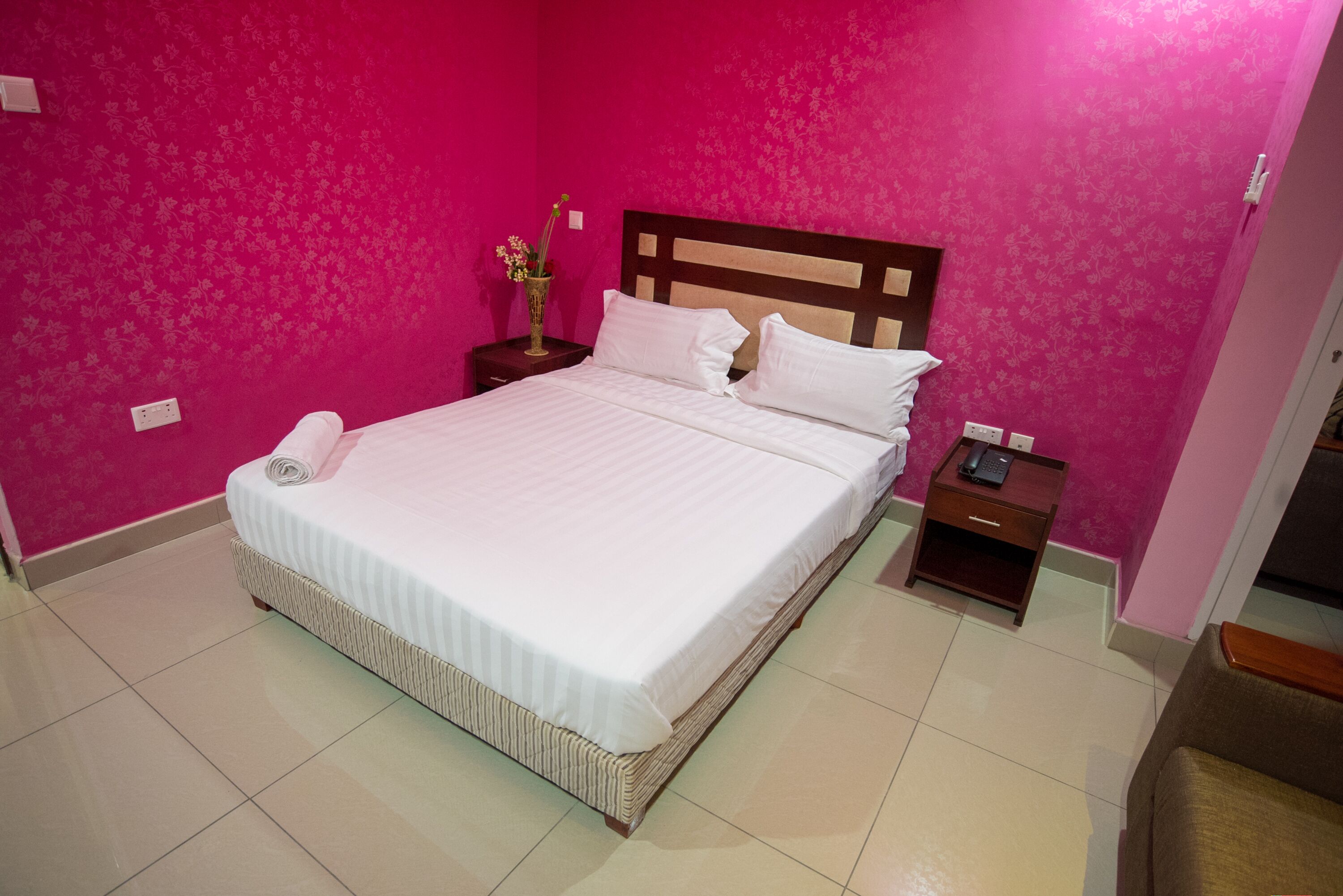 A neatly made bed in a room with pink walls and a wooden headboard.