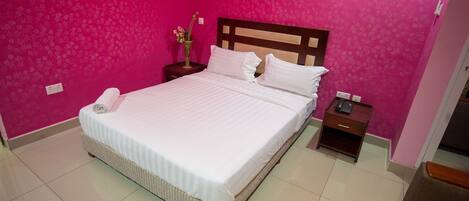 A neatly made bed in a room with pink walls and a wooden headboard.