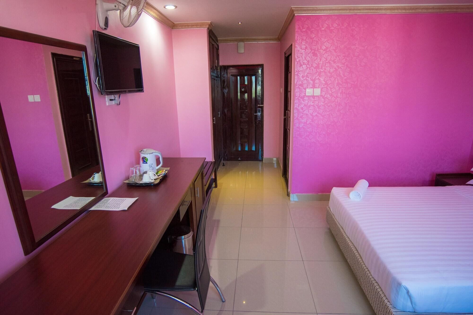 Una habitación de hotel con escritorio, cama, televisor y puerta que da a otra habitación.