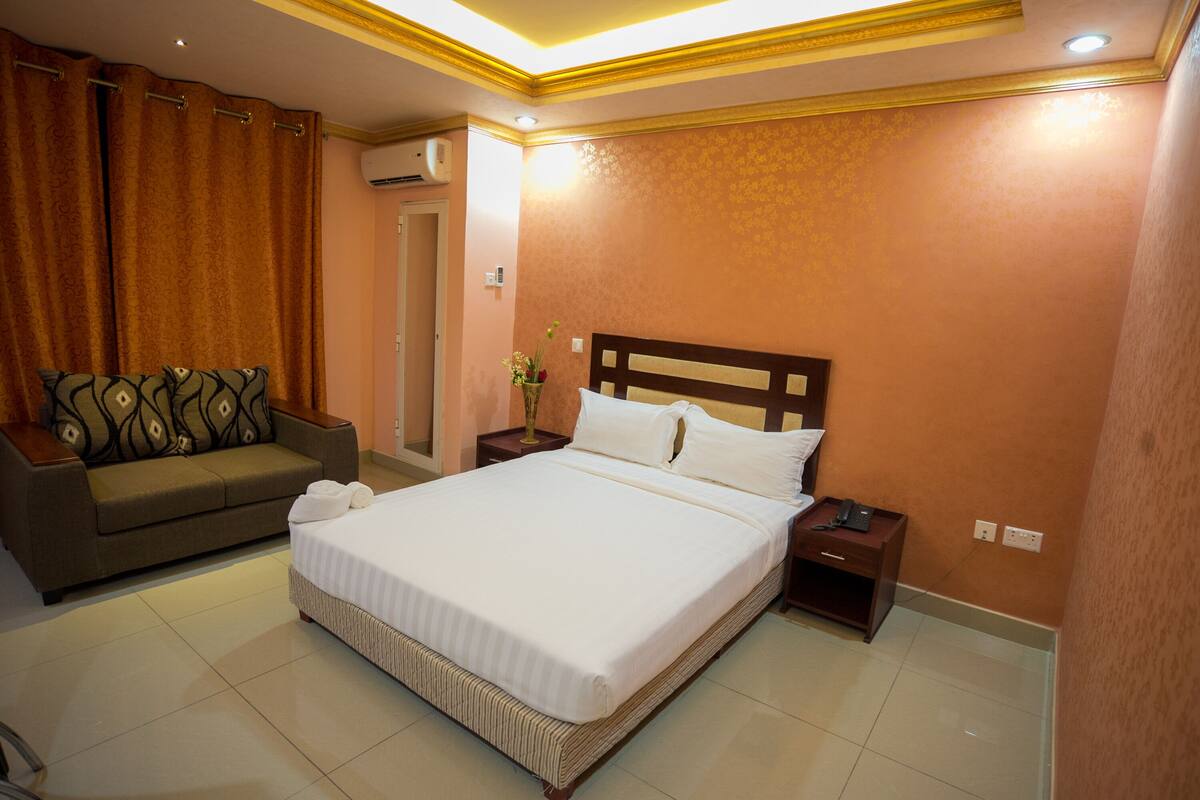 Une chambre d’hôtel avec un grand lit, un canapé, une table de chevet et un climatiseur fixé au mur.