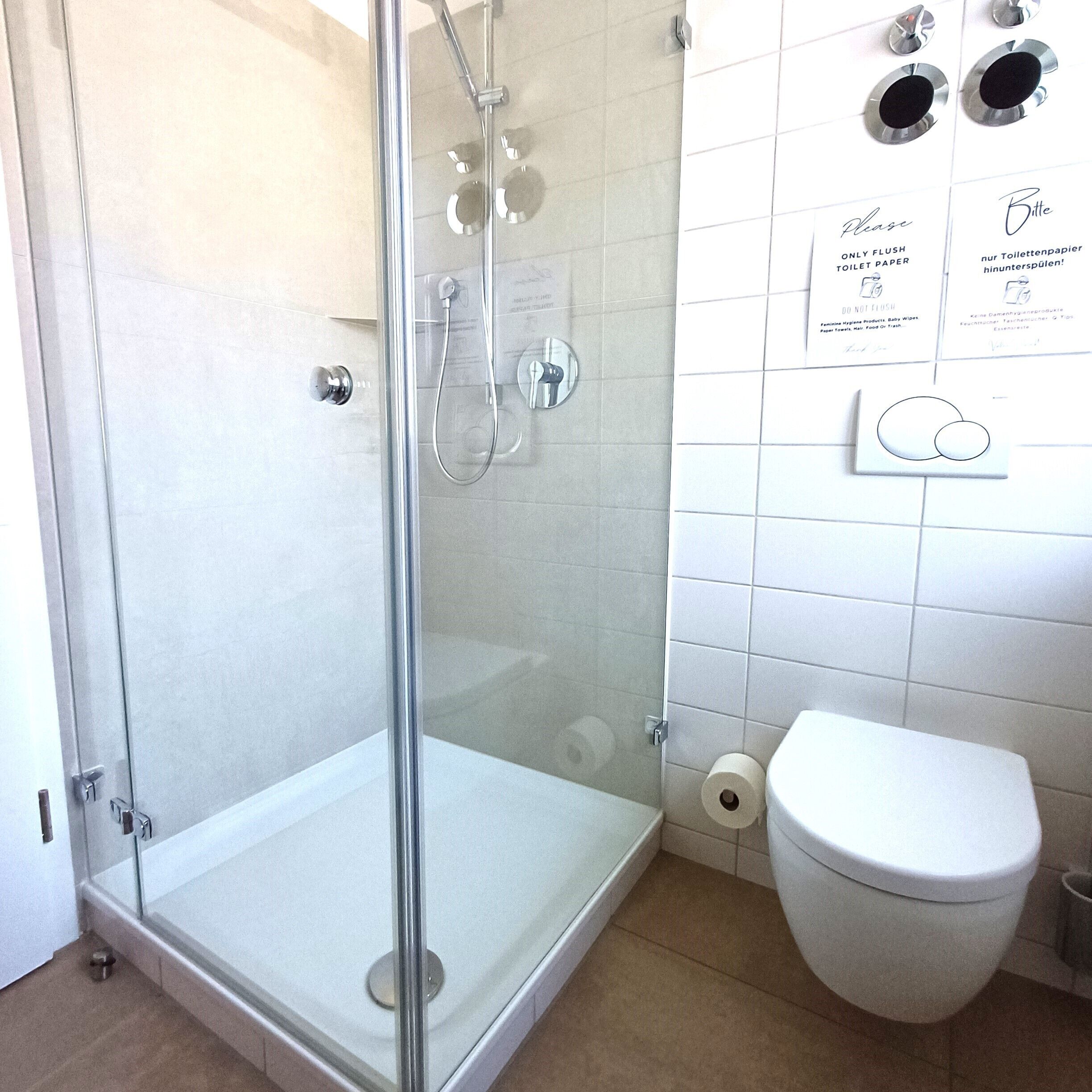 A bathroom with a glass-enclosed shower, a white toilet, and a wall-mounted toilet paper holder with multilingual instructions.