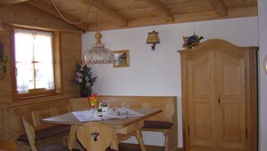 Un comedor con una mesa y sillas de madera, una araña, un armario y un ventanal con cortinas.
