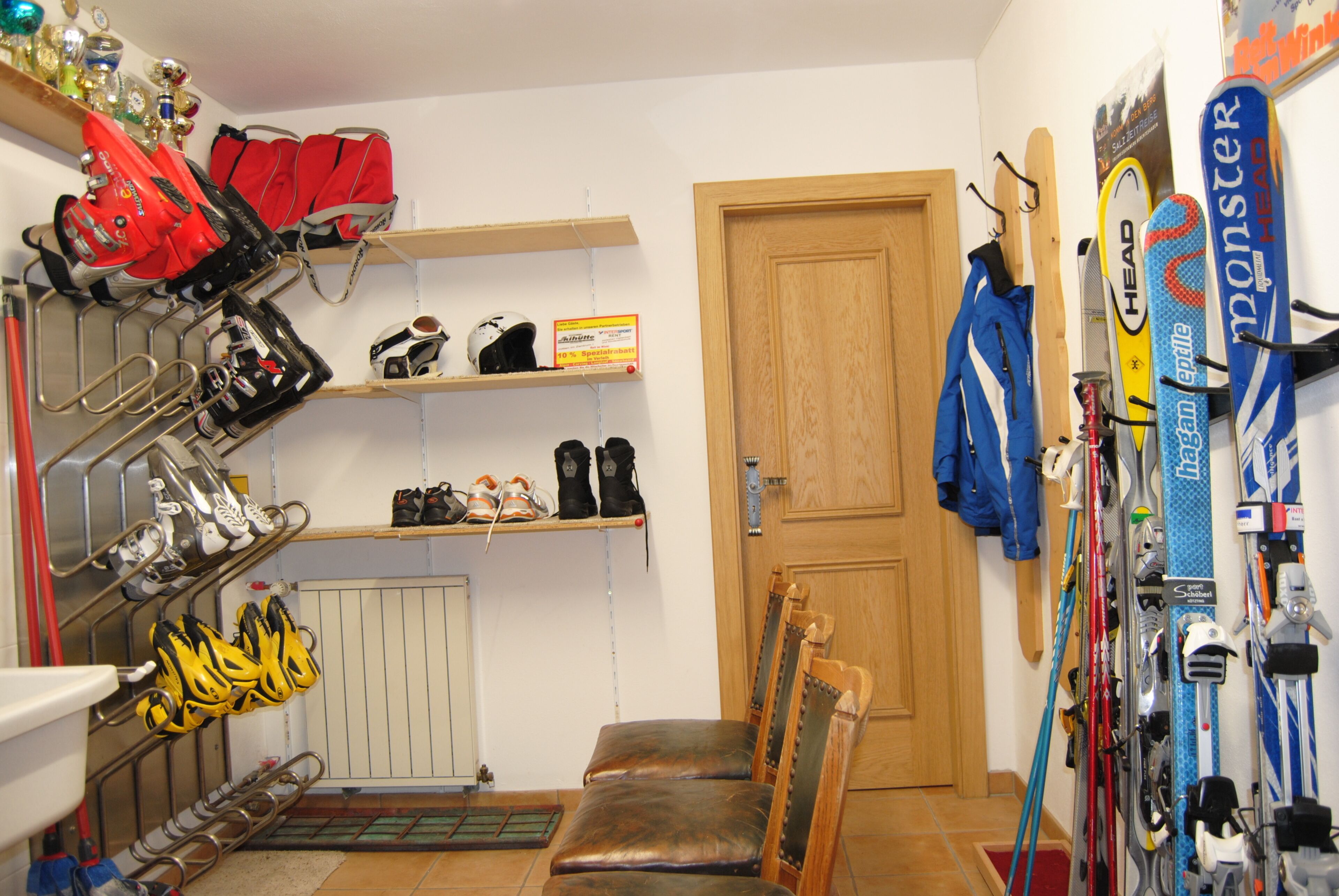 Ein Skiabstellraum mit Regalen für Ski und Stiefel, einer Holztür und einem Stuhl.