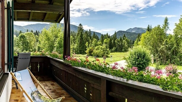 Un balcon donnant sur un jardin luxuriant et sur les montagnes.