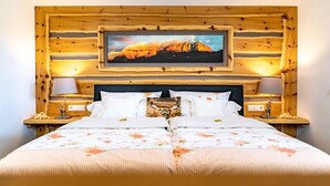 Un lit double avec une literie à motifs floraux, deux lampes de chevet, une tête de lit en bois ornée d’un tableau encadré et un lambris en bois.