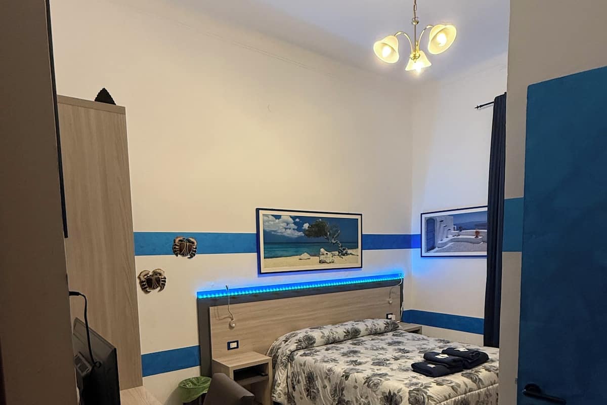 A bedroom with a bed, a desk, a chair, a TV, and a ceiling light.