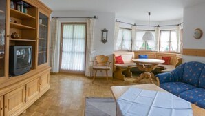 Een gezellige woonkamer met een houten kast, een televisie, een houten stoel, een ronde tafel en een blauwe bank.