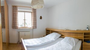 Een slaapkamer met een bed, nachtkastje, raam met gordijnen, radiator en een houten hoofdbord.