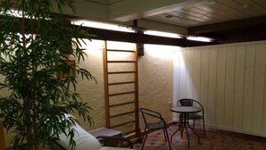 Een kleine kamer met een bed, een stoel, een tafel en een kamerplant.