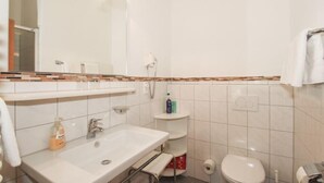 Kylpyhuone, jossa on pesuallas, peili, wc ja hyllyjä, joilla on hygieniatuotteita.