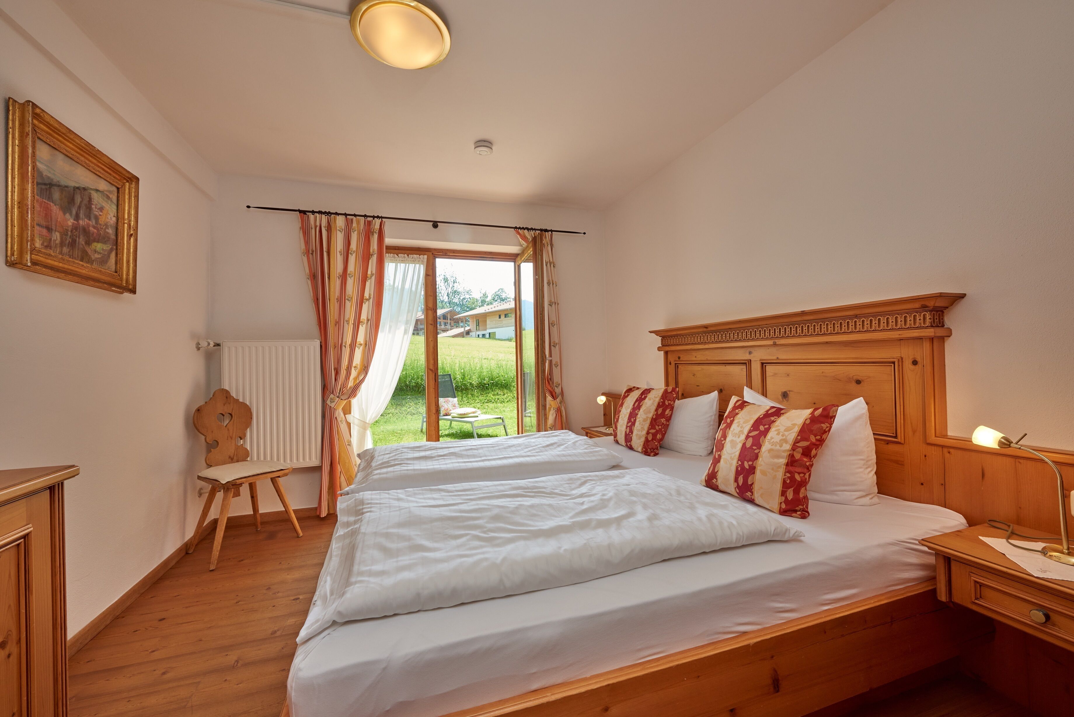 Een slaapkamer met een groot bed, een houten hoofdeinde en uitzicht op een tuin door een raam.