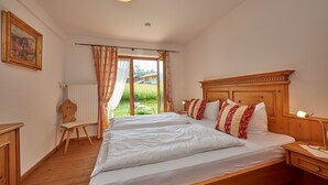 A bedroom with a large bed, wooden headboard, and a view of a garden through a window. - Ferienwohnung (9) (Reit im Winkl)
