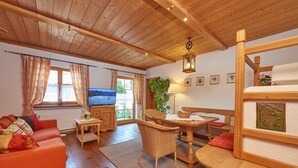 A cozy living room with a wooden ceiling, a television, a sofa, a dining table, and a bench. - Ferienwohnung (9) (Reit im Winkl)