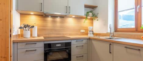 Una cocina moderna con armarios blancos, horno empotrado y ventana con vista a un paisaje nevado.