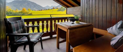 A wooden balcony with a view of mountains, a table, and two chairs.