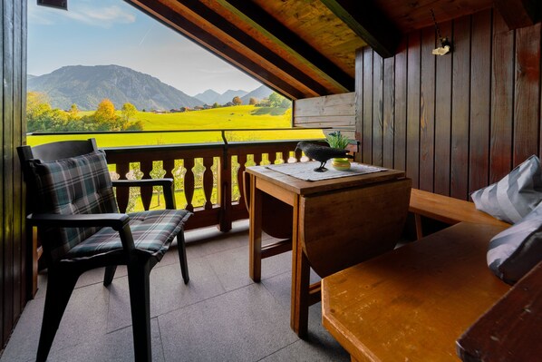 A wooden balcony with a view of mountains, a table, and two chairs.