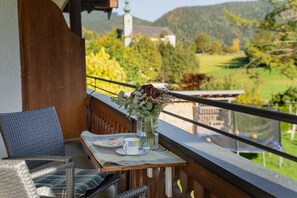 Ein Balkon mit Korbmöbeln, einem Tisch mit Blumen und einem schönen Blick auf eine Kirche und Grünflächen.