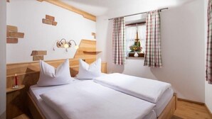 A room with two beds, wooden headboard, a nightstand, a wall clock, and a window with curtains.