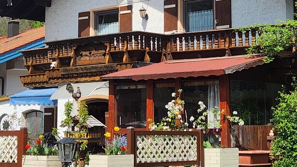 A traditional building with a sign reading "Neuhäusl". It features a balcony with wooden railings and a red awning. - Apartment Rauschbergblick 80 sqm, 2 separate bedrooms, bathroom, eat-in kitchen (Ruhpolding)