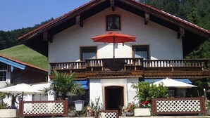 A two-story building with a balcony, a red umbrella, and outdoor seating. - Apartment Rauschbergblick 80 sqm, 2 separate bedrooms, bathroom, eat-in kitchen (Ruhpolding)