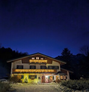 A two-story building with a balcony, a Christmas tree, and a snow-covered ground.