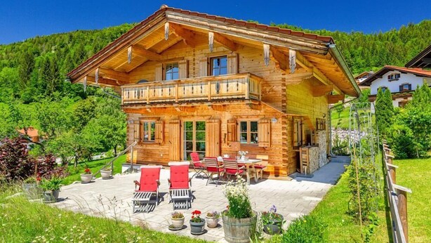 Eine Holzhütte mit Balkon, Sitzgelegenheit im Freien und einem Garten.