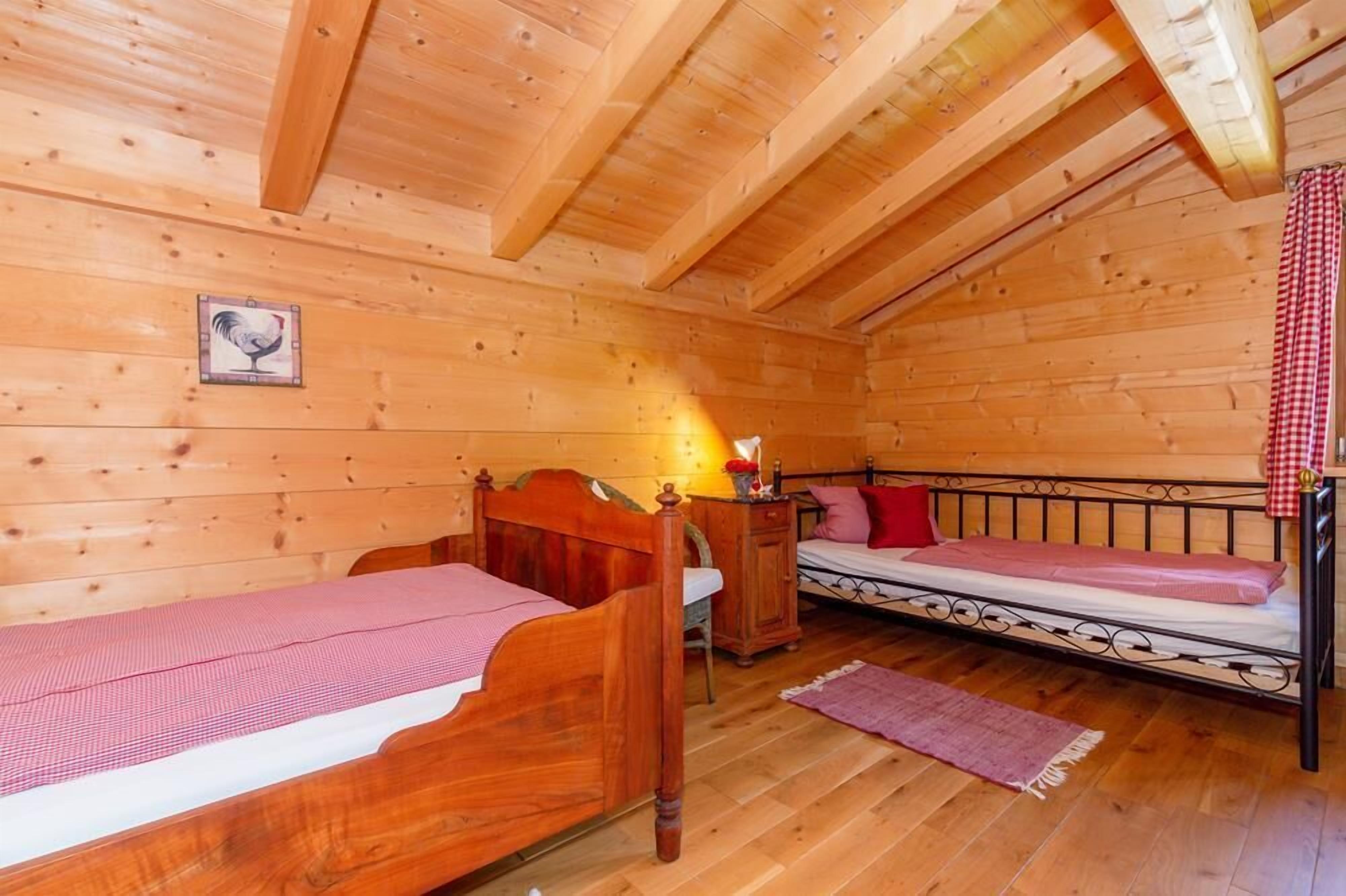 Une pièce chaleureuse, aménagée dans un chalet en bois, avec deux lits en bois, une petite table et un tableau accroché au mur.