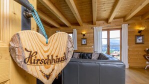 Ein Holzinnenraum mit einem herzförmigen Schild mit der Aufschrift 'Kirschhaus' und einem grauen Sofa.
