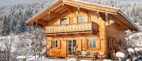 Una cabaña de madera con balcón, rodeada de árboles nevados y un cielo despejado.