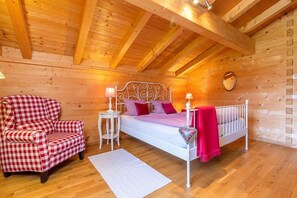 Een gezellig houten slaapkamer met een bed, een geruit fauteuil en een klein nachtkastje.